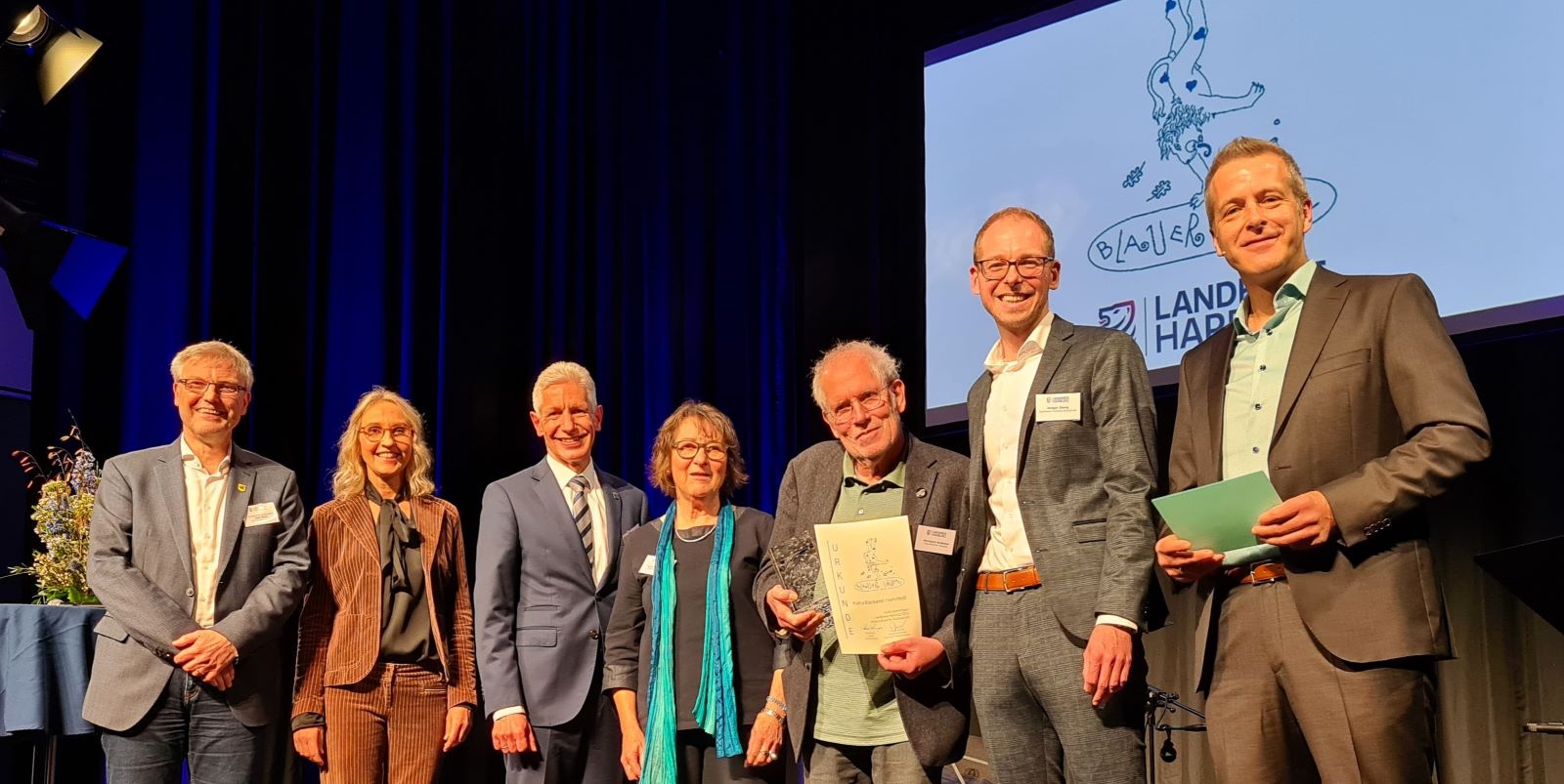 Olaf Muus (Bürgermeister der Samtgemeinde Hanstedt), Katja Hahne (ehemalige Sozialarbeiterin einer Flüchtlingsunterkunft in Hanstedt), Rainer Rempe (Landrat Landkreis Harburg), Lore Ruckdeschel (Ehefrau und Unterstützerin von Hermann Krekeler), Hermann Krekeler (Preisträger und Initiator der KulturBäckerei Hanstedt), Holger Iborg (Förderer und Vorstandvertreter der Sparkasse Harburg-Buxtehude) und Christoph Reise (Moderator). Foto: FLMK